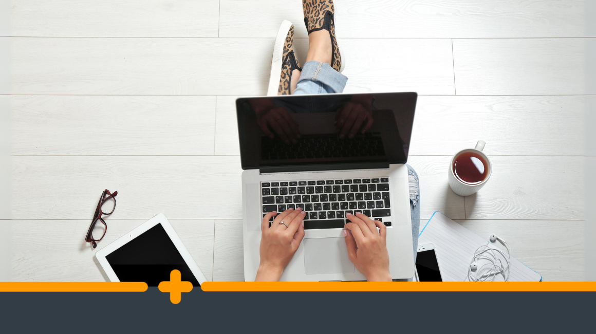 Widok z góry na zorganizowane stanowisko pracy osoby pracującej na laptopie, otoczoną kawą, tabletem, kawa i słuchawkami na jasnej podłodze