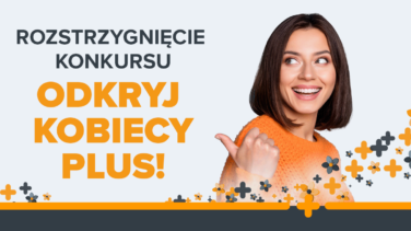 Uśmiechnięta kobieta w pomarańczowym swetrze pokazuje kciukiem na napis "Odkryj kobiecy plus"
