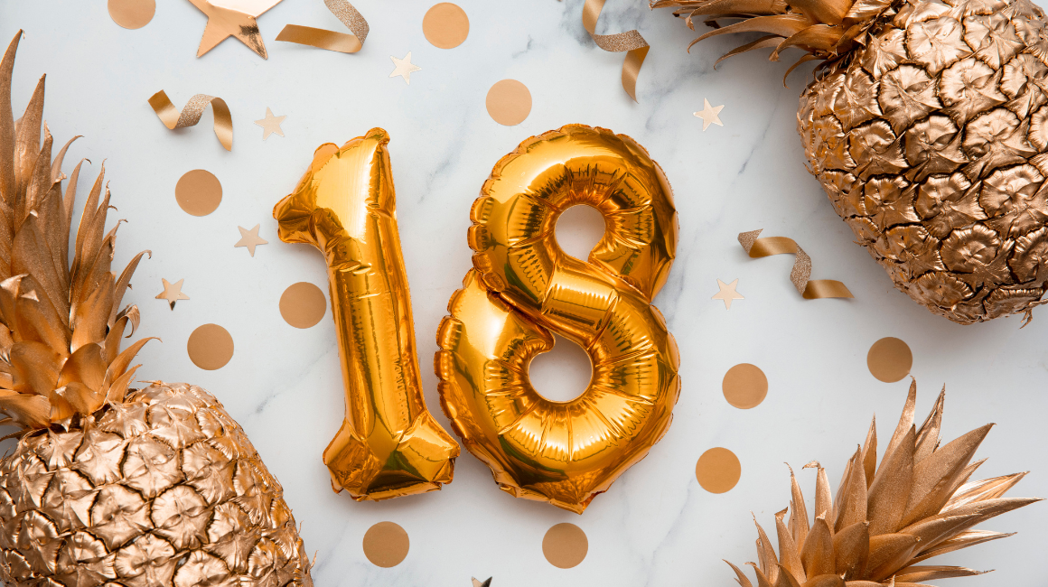 Dekoracja urodzinowa z balonami w kształcie liczby 18, złotymi ananasami i konfetti na jasnym tle